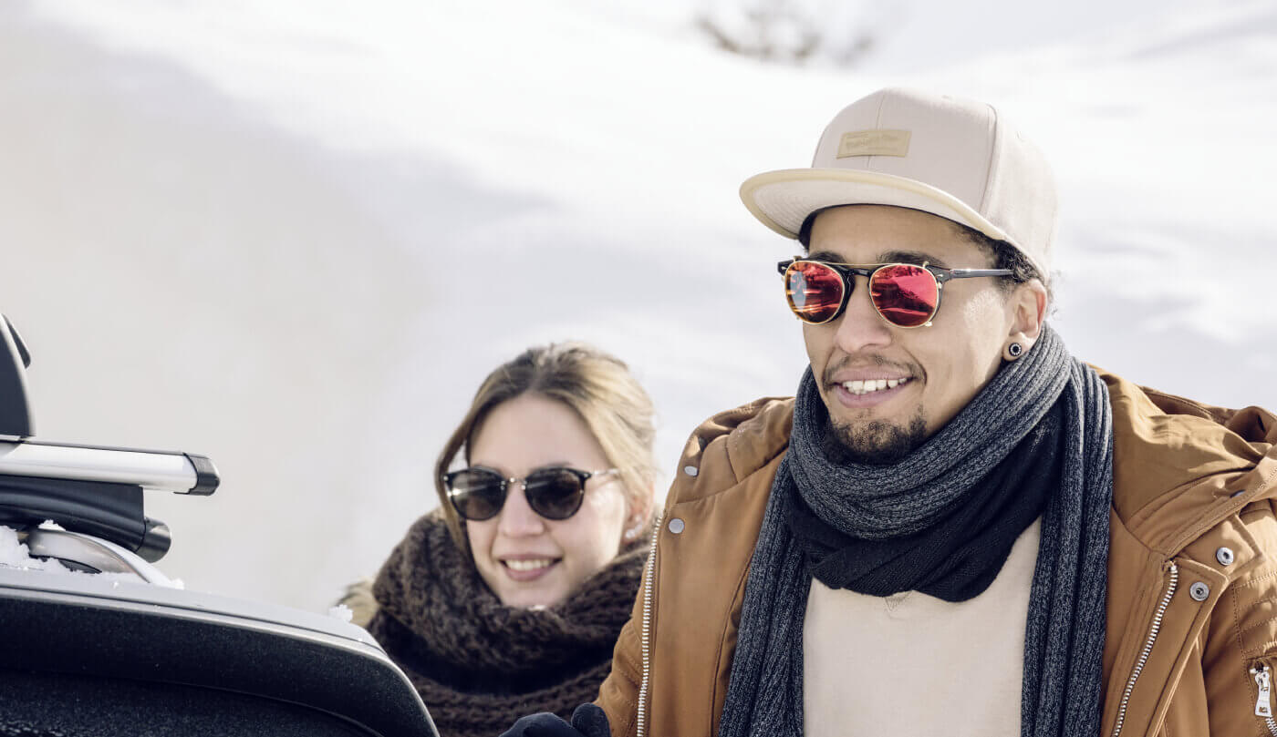 Smiling couple in winter jackets beside snow-covered car